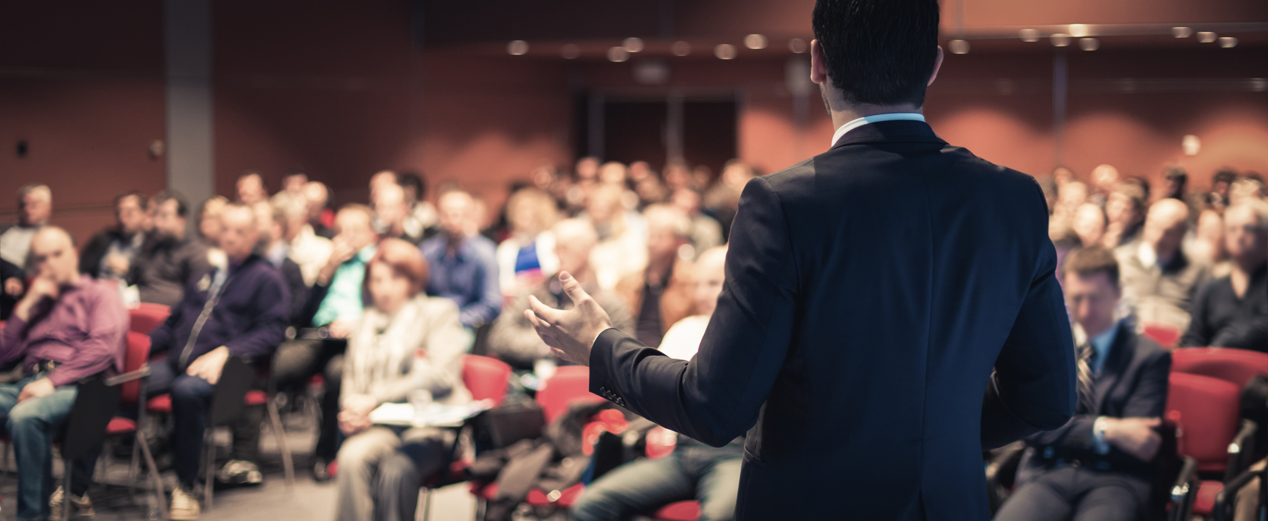 Speaker Giving a Talk in Conference Hall at Business Meeting Event. Rear View of Unrecognizable People in Audience at the Conference Hall.